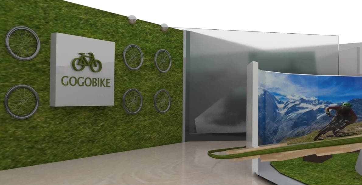 3D render of the GOGOBIKE exhibition entrance: a grass-covered wall with logo panel and mounted bicycle wheels beside a frosted glass partition