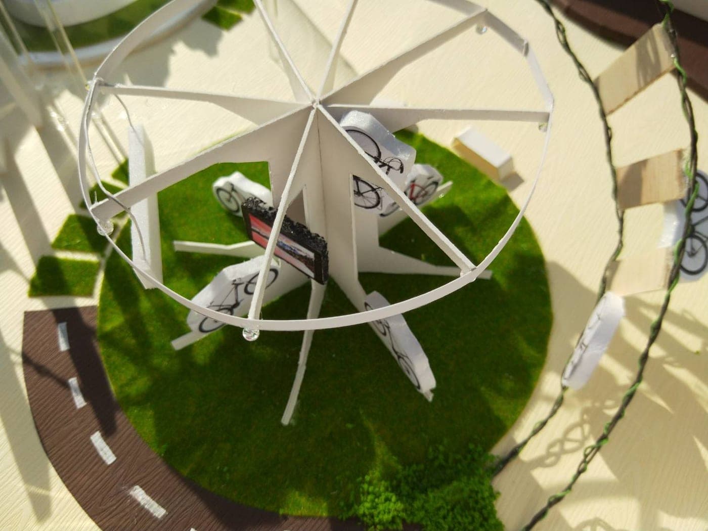 Close-up of the GOGOBIKE scale model's white paper wheel structure displaying miniature bicycle cutouts on a green turf circle