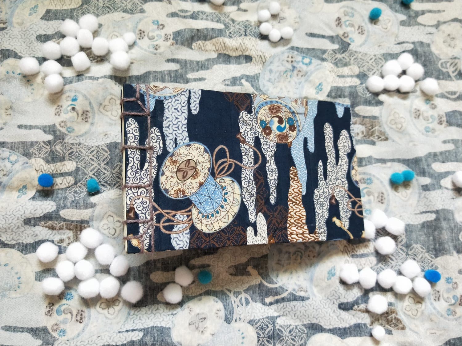 Handbound notebook covered in navy Japanese-print fabric lying on patterned cloth, with exposed grey yarn chain stitching along the spine.