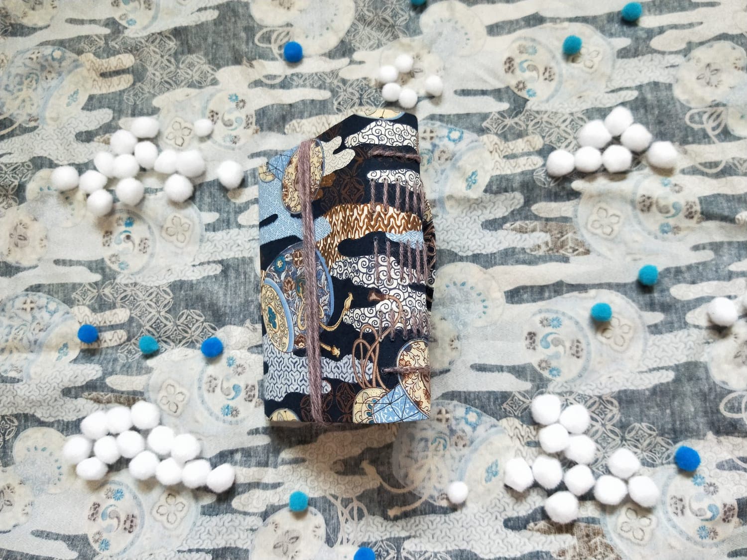 Small handbound book in navy Japanese-print fabric with rows of parallel grey yarn stitches along the spine and a wrap-around yarn tie.