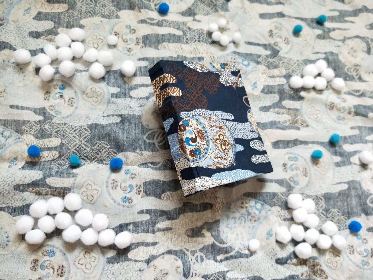 Hardcover case-bound book covered in navy Japanese-print fabric standing at an angle on matching patterned cloth.