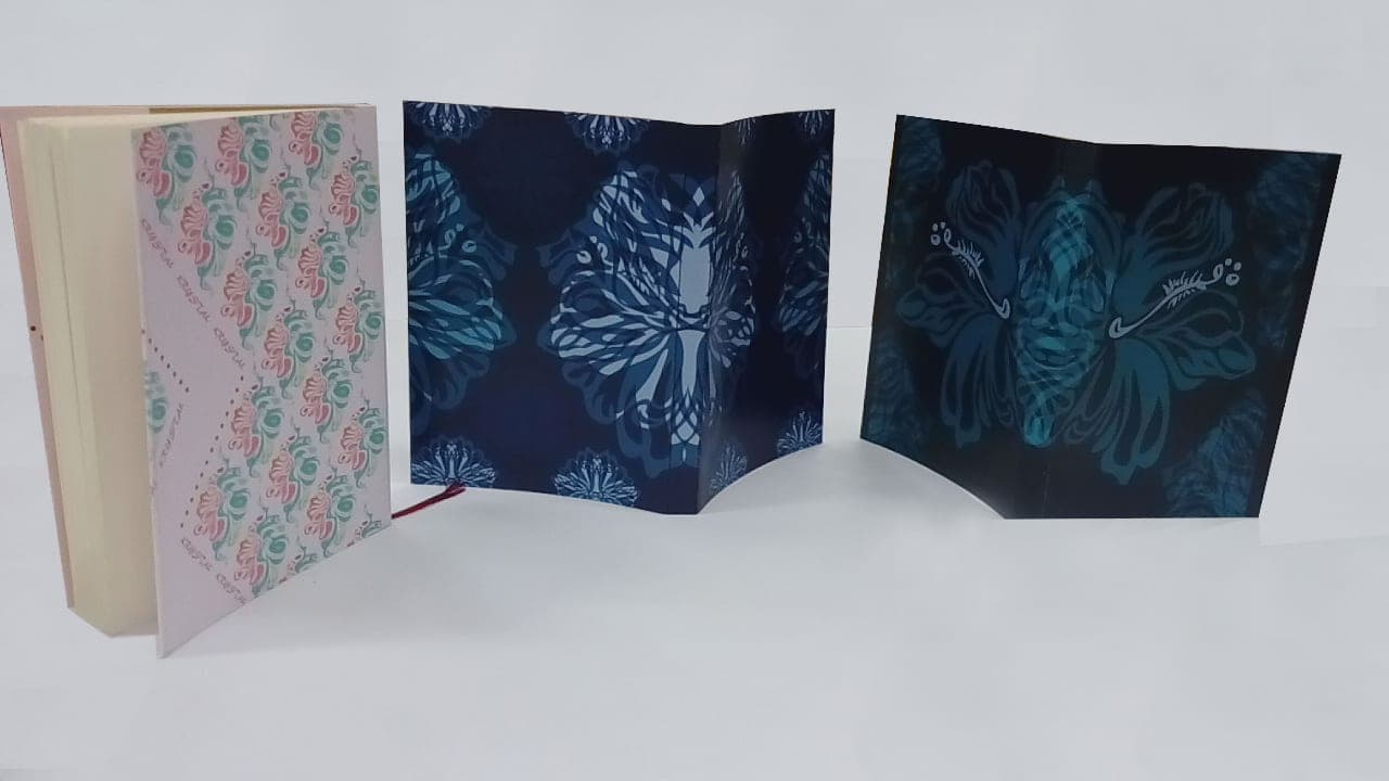 Three handmade leaf-pattern notebooks standing with covers opened, shown from a lower angle.