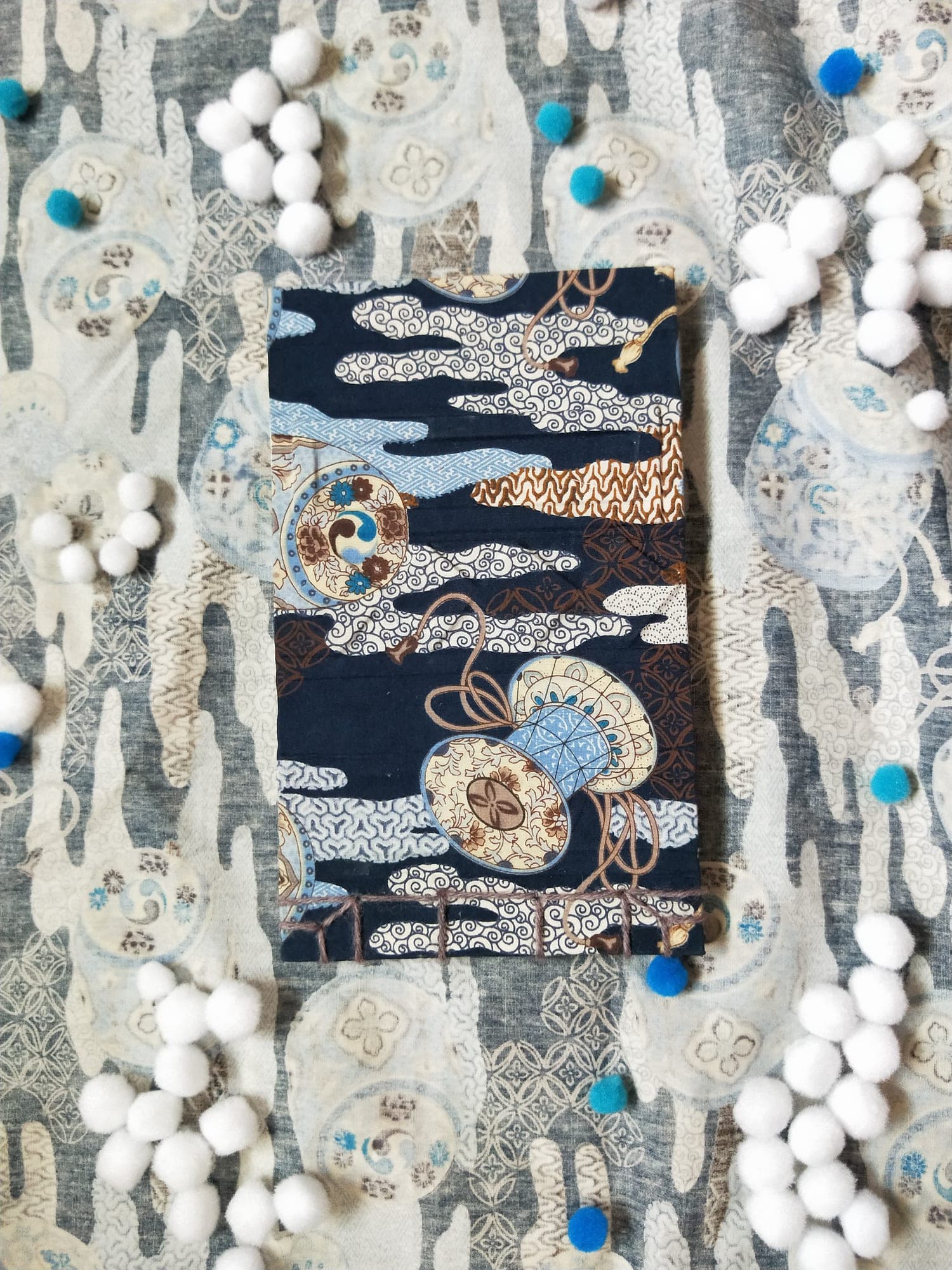 Handbound notebook in navy Japanese-print fabric lying flat on matching cloth, grey stitching exposed along the lower spine edge.