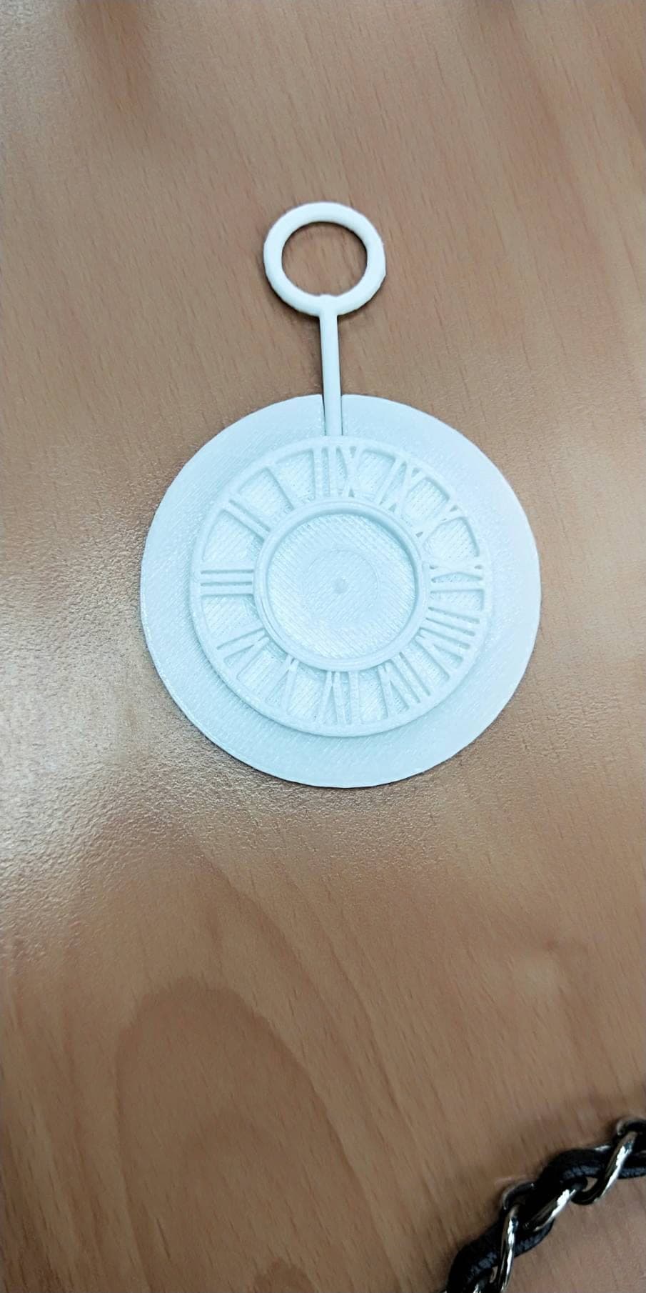 A 3D-printed white pocket-watch keychain with Roman numerals, photographed on a wooden desk