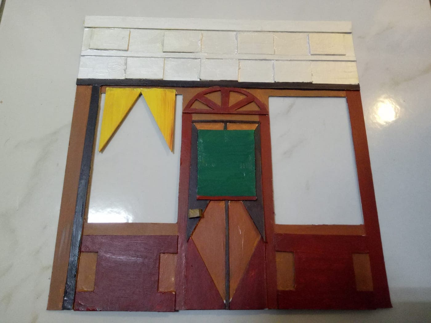 Finished handmade miniature shop facade with white brick cornice, yellow curtains in one window, and a central door with green panel under an arched fan transom.