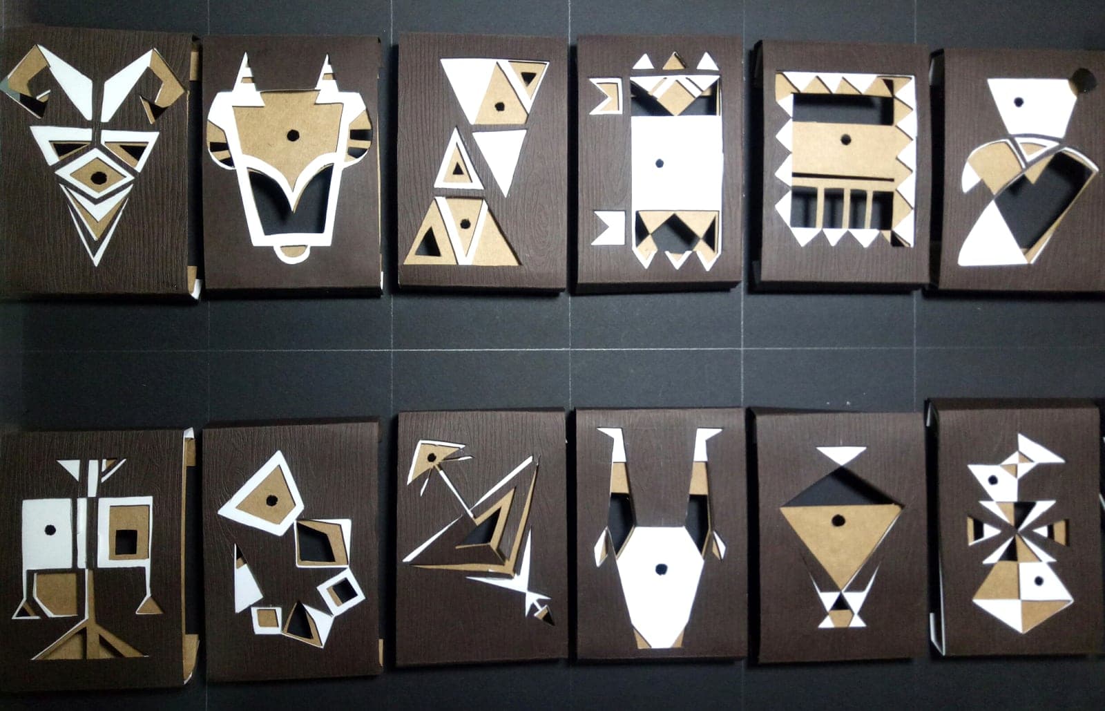 All twelve zodiac chocolate boxes laid out in two rows: dark wood-textured paper with kraft and white geometric cutouts of each sign